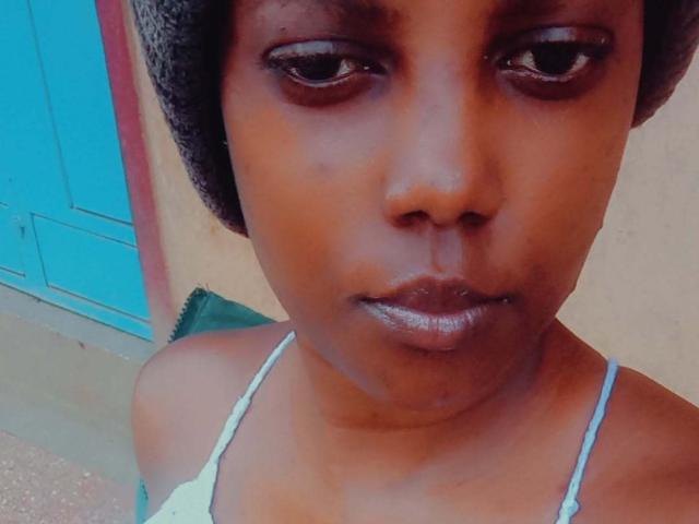 Starlesty with dark brown skin, wearing a gray headwrap and light blue spaghetti strap top, has shiny lips and a serious expression, her tits are small and her pussy is unseen.