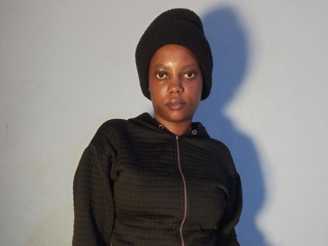 Starlesty with dark brown skin, wearing a black knit beanie and black ribbed zip-up hoodie, has small, round, puffy ass, and a serious, slightly curious expression.