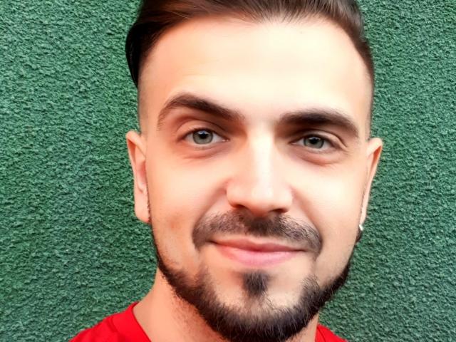 JaceThorne has a smooth face, light green eyes, short brown hair, and a trimmed beard with a small mustache. He's wearing a red shirt and smiling subtly.