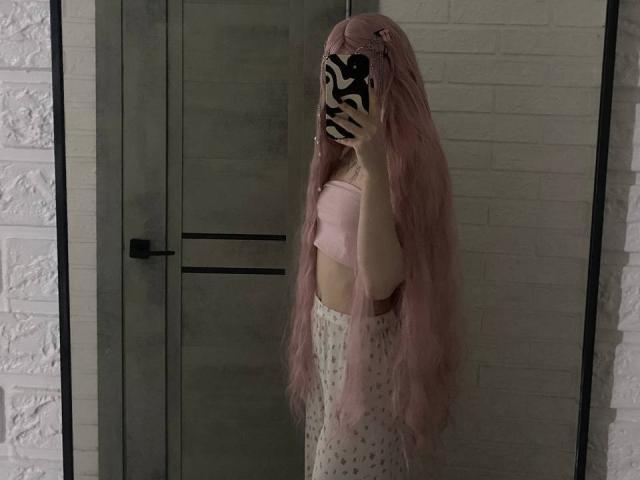 KirstieDevost with long pink hair, wearing a pink tube top and high-waisted patterned pants, taking a mirror selfie, zebra-pattern phone case, white brick walls, gray door.