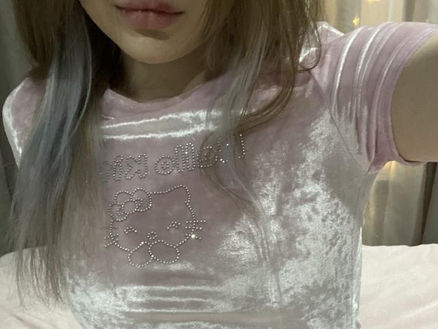 KirstieDevost in a pink velvet shirt with silver floral studs, showing her tits, with long grayish-brown hair, slightly parted lips, and a soft, warm light.