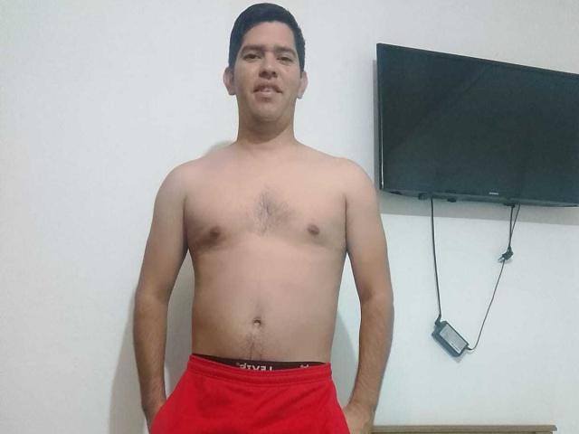 ChristopherRusso, shirtless, medium build, light skin, short black hair, small chest, red underwear, hands in pockets, standing, flat stomach, slight chest hair, TV mounted on white wall behind.