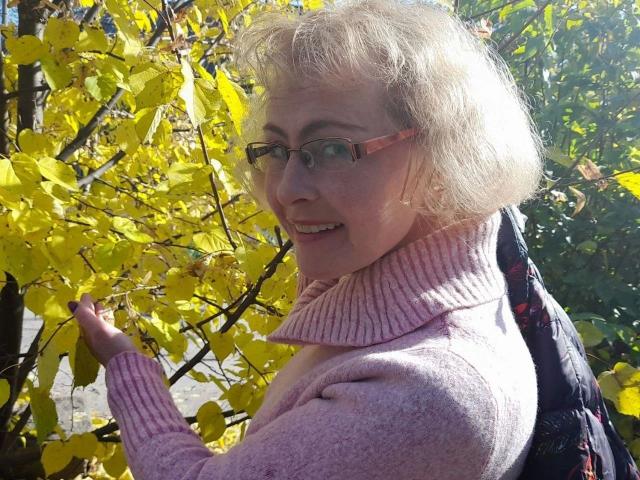 SunnySoul-hot with blonde hair, glasses, pink sweater, and backpack, smiling while touching yellow leaves. She's got small tits and a cute, happy face. Sunlight filters through.