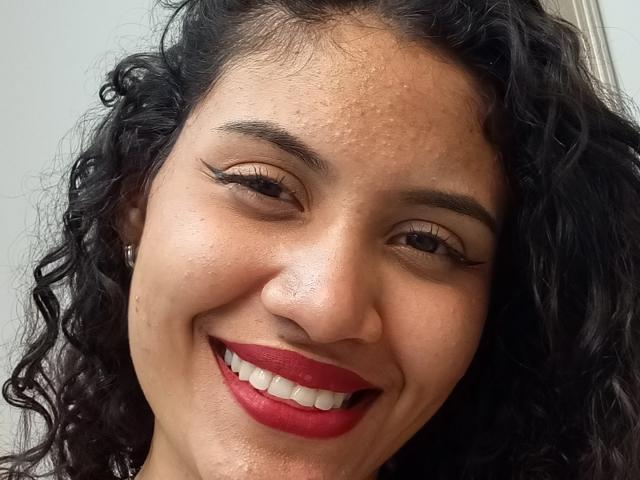 ValeryPoleth has curly black hair, brown eyes, and red lipstick. She's smiling with white teeth, wearing eyeliner, and has a small beauty mark near her right cheek.