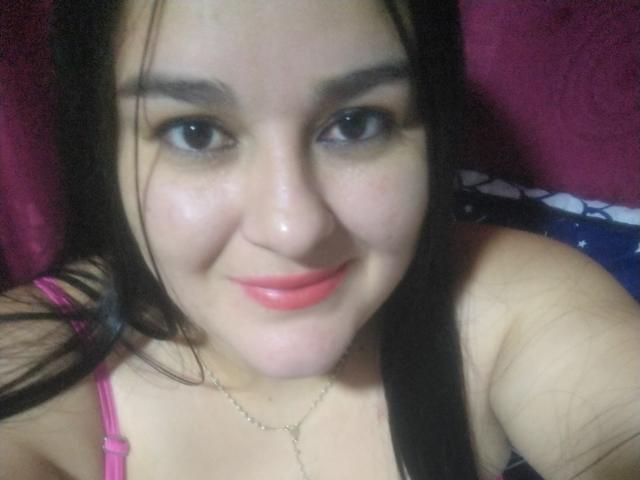TessieMira has a cute face with dark eyes, pink lipstick, and black hair, wearing a pink top with thin straps, showing a slight smile. She's looking at the camera.