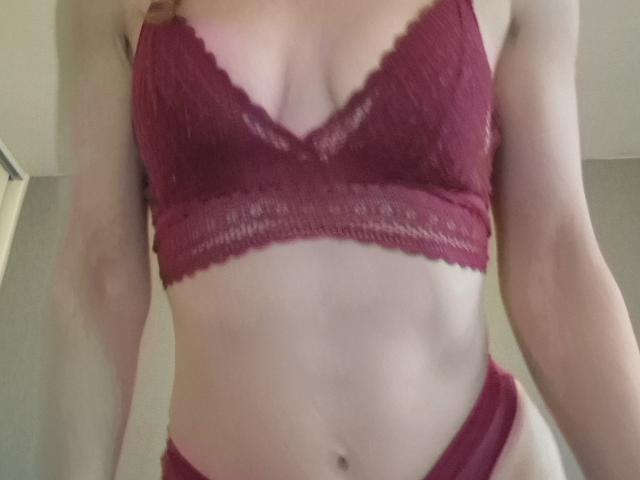 FrancaiseAline in red lace lingerie, showing her tits in a bra and matching panties, with a slight view of her flat, toned stomach and pale skin.