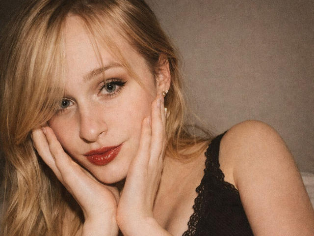 FlyFreedom with blonde hair, blue eyes, and red lipstick, hands on cheeks, wearing black lace lingerie, looking cute and sexy, soft lighting, subtle smile, gentle expression.