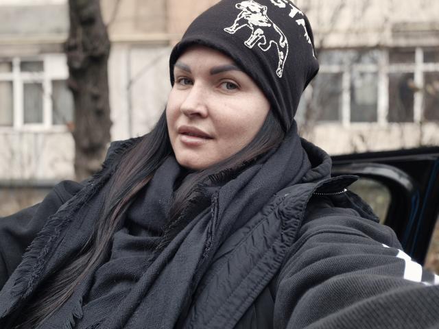 GeorgiaLerox with long black hair, wearing a black beanie with white skeleton design, black scarf, and black jacket, smiling slightly, taking a selfie, showing her face and upper body.