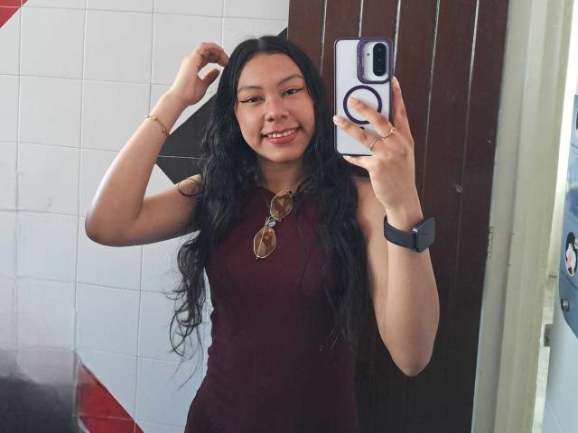 IvyMontaner with long black hair, smiling, wearing a maroon dress, sunglasses on chest, black wristwatch, holding phone, raising arm, mirror selfie, visible butt, medium breast size.