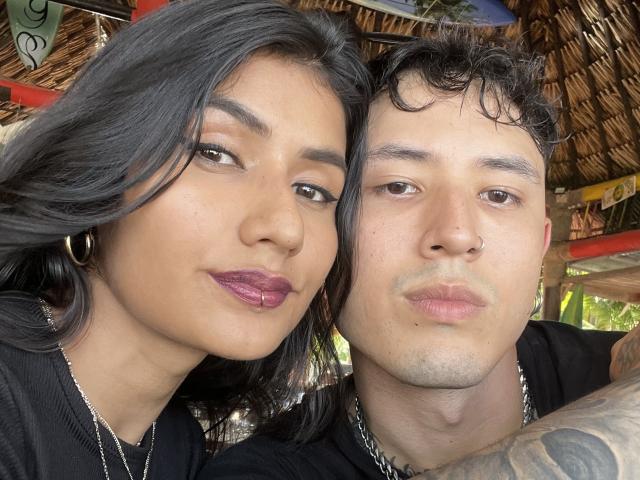 TheJoestars with dark hair and purple lipstick, and TheJoestars with short curly hair and a nose ring, both pouting at the camera, wearing black shirts and chain necklaces.
