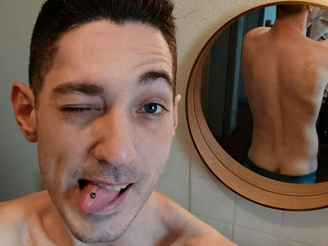 FrancaisH has short brown hair, winks with one eye, sticks out tongue with a piercing, and shows a mirror reflection of his bare back and blue underwear.