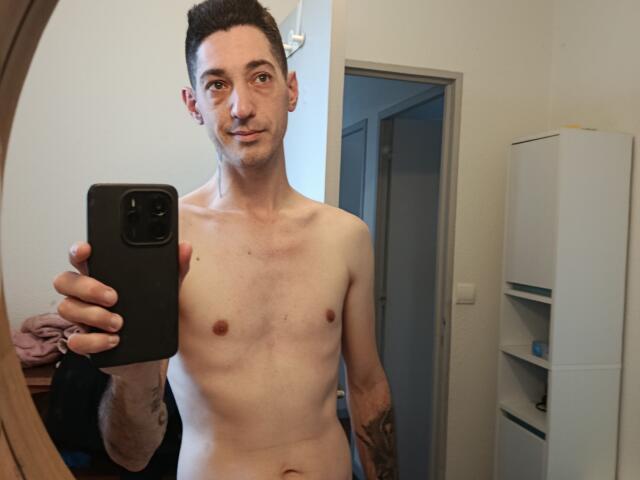 FrancaisH is a slim, shirtless guy with short dark hair, small nipples, tattoos on his right arm, and a nose ring, taking a mirror selfie with a black phone.