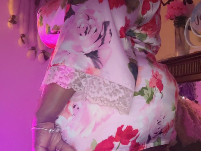 DrippnChocolate's butt is shown from behind, wearing a floral pink and red dress with lace trim, dark skin, and pink lighting, holding a pink handbag on the right.