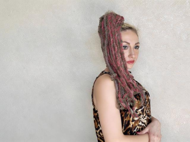 LilaniLoverX with pink and brown braided ponytail, leopard print dress, arms crossed, red lipstick, white textured wall background, looking at camera with slight smile.