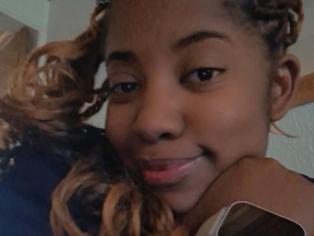 CynthiaRamos has dark brown skin, curly blonde and brown hair, and a slight smile. Her brown eyes and soft pink lips are visible. She rests her cheek on her hand.