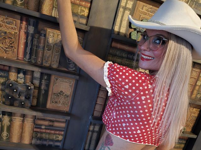NinaNicoleRoyale with long blonde hair, red polka dot top, white hat, glasses, smiling, reaching for books, showing tattoo on right side, cute, attractive, blonde, small tits.