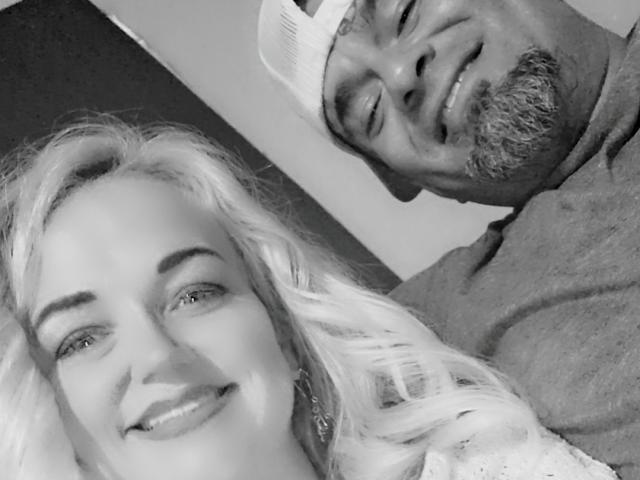 Black man with beard and cap, smiling, next to HIMandHER with long blonde hair and earrings, both in grayscale selfie. HIMandHER has small nose and subtle smile.