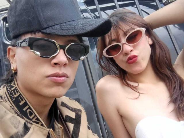 FeviceFabinLm with black cap, hexagon sunglasses, and tan jacket, next to FeviceFabinLm with pink cat-eye sunglasses, red lips, and white strapless top, showing tits.