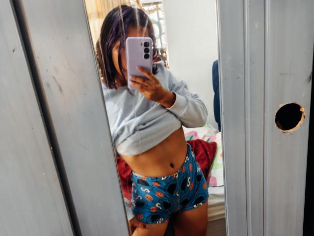 HattyMollie in blue cartoon print shorts, lifting a gray sweater to show her toned midriff, taking a mirror selfie with a purple phone. Her ass is slightly visible.