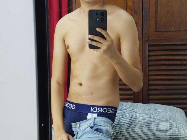 KevinCharles, shirtless, holding phone, wearing dark blue boxer shorts, jeans partially down, mirror selfie, visible ass, slightly tan skin, medium build, short dark hair, wooden door background.