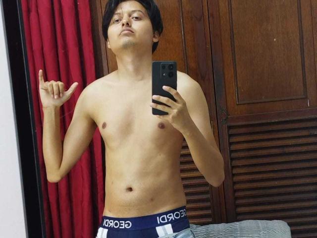 KevinCharles, shirtless, holding phone, middle finger up, wearing dark blue boxer briefs with white and gray stripes, standing in front of mirror, short black hair, slightly annoyed expression.