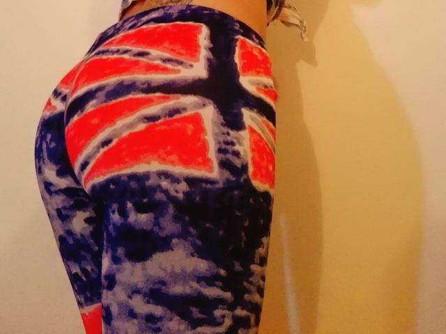 AnneSensu's ass in tight, colorful, tie-dye leggings with red, white, and blue Union Jack pattern, standing against a beige wall, showing her butt and lower back.