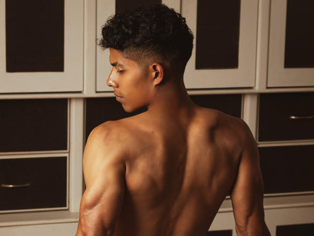 VictoryCassus, shirtless with curly black hair, has a toned, muscular back and brown skin. He's looking to the side, showing a strong, attractive profile.
