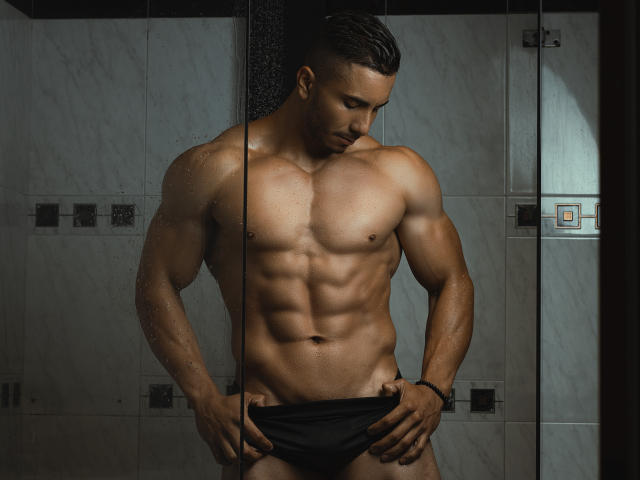 ZaneMaverick, musculoso, sem camisa, em pé no chuveiro, abaixando a roupa íntima preta, mostrando abdominais definidos, pele molhada, cabelo curto e escuro, olhando para baixo, mão direita na cintura, mão esquerda segurando a roupa íntima..