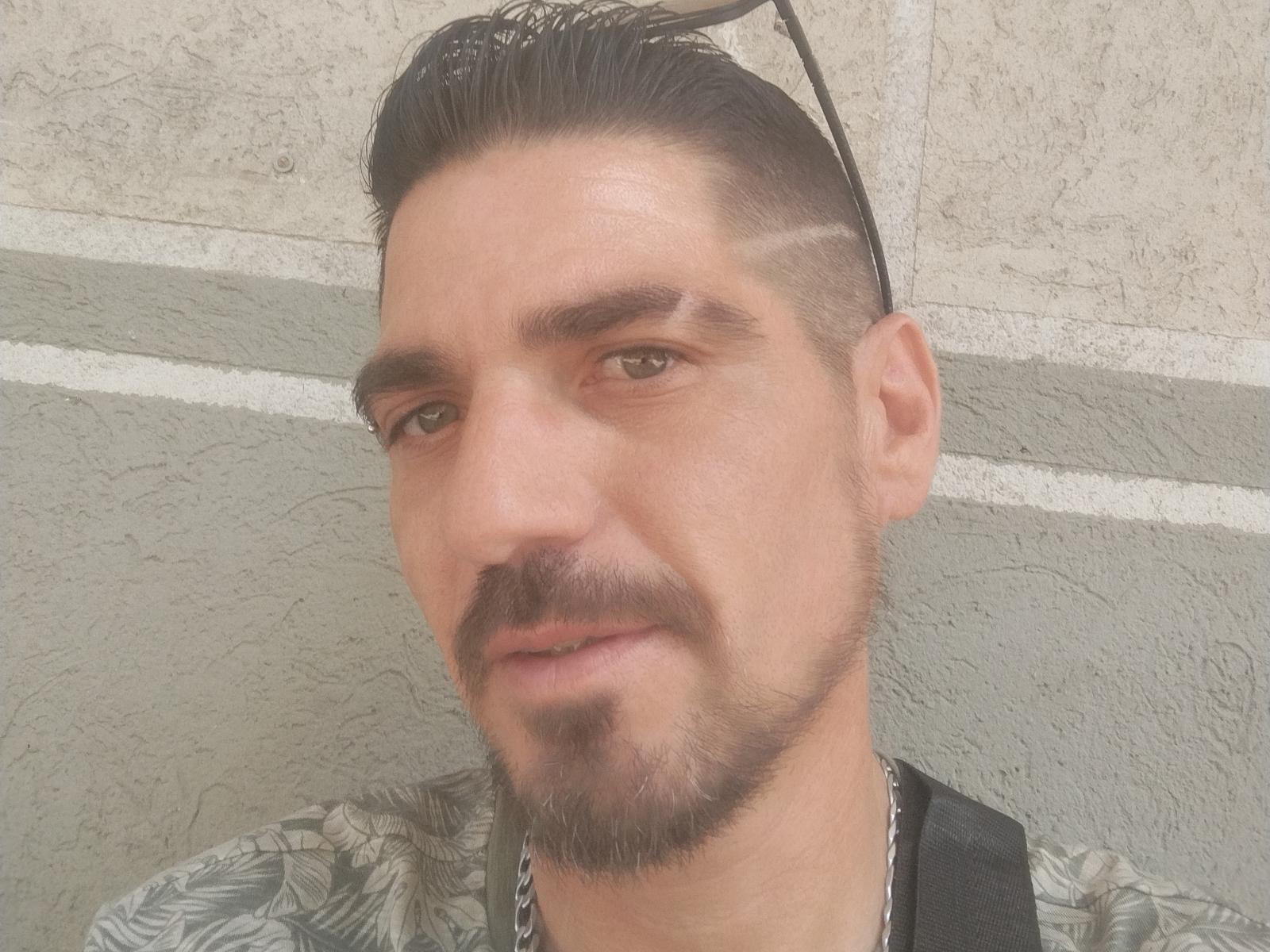 Chinchetalove has a medium skin tone, dark hair with a undercut, a thin mustache, and a goatee, wearing a patterned shirt with sunglasses on his head.