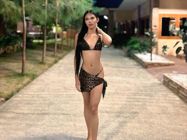 CassandraWise, with long black hair, wearing a leopard print bikini, showing her small tits and slim ass, stands confidently on a concrete path at night.