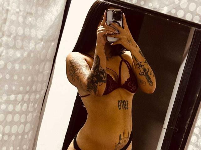 JessiParker taking a mirror selfie in dark red lingerie, showing multiple tattoos on her arms and lower belly, with her phone covering her face. Her tits are medium-sized.