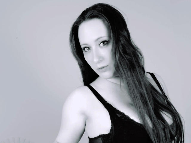 LaviniaJolie-hot with long, dark hair, wearing a black lace bra, has pale skin, and a seductive, half-smiling look in a grayscale, high-contrast image.