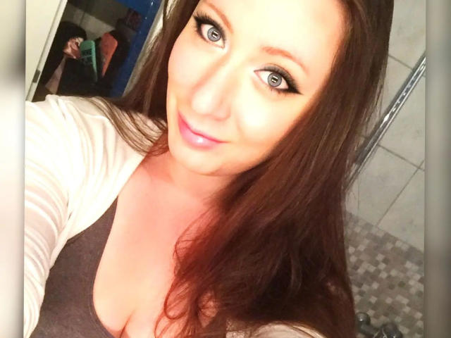 LaviniaJolie-hot has blue eyes, long brown hair, and a pink smile. She's wearing a gray top with a white cardigan, showing her boobs in a selfie.