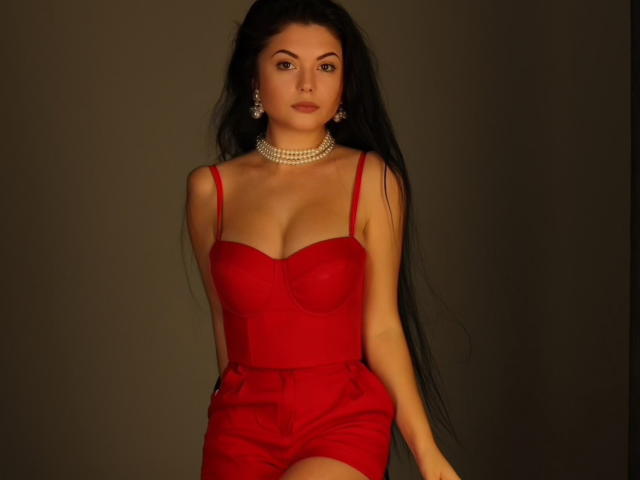 XKleo in a red dress with a low-cut top, showing her tits, wearing high-waisted red shorts, a pearl necklace, and dangling earrings, with long black hair.
