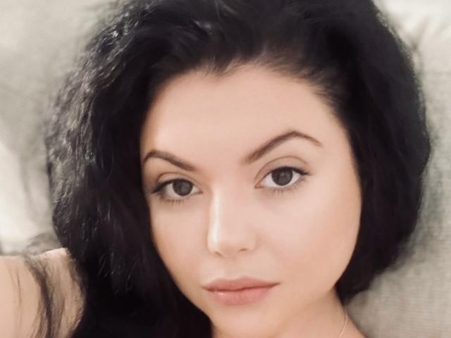 XKleo has black, wavy hair, light skin, and brown eyes with a subtle, neutral expression. Her full lips are slightly parted. She's looking directly at the camera.