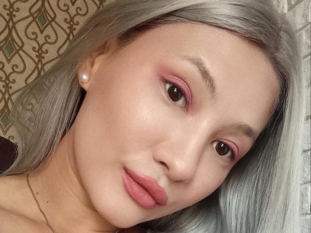 DamelySakura's face with pale skin, pink eyeshadow, and silver hair, wearing a pearl earring, and pink lipstick, looking slightly to the side with a subtle smile.