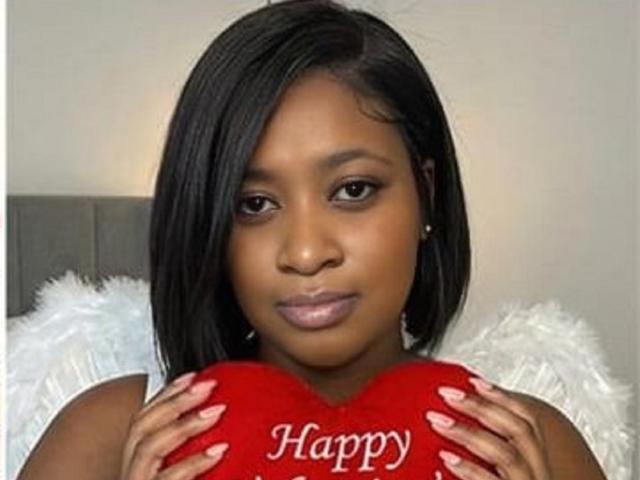 AnyBigAssForU with dark skin, straight black hair, and pink lips, holding a red heart with "Happy" in white, wearing white fluffy angel wings.