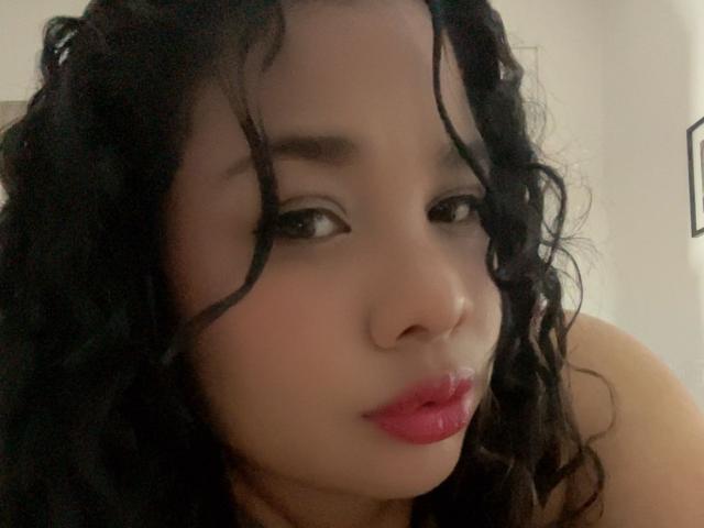 VanessaFory has curly black hair, full pink lips, and dark eyes, with a light skin tone, looking slightly to the side with a subtle, sexy expression.