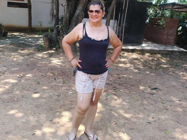 AdrianaPrettie has a chubby butt, big tits in a black tank top, and her white shorts are pulled down, showing her pussy. She's wearing sunglasses and standing outside.