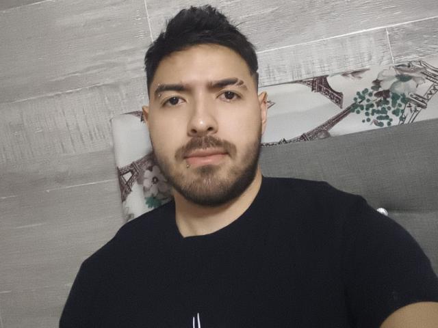 AlecAndAndrus has a short, dark beard, black hair, and a nose ring. He's wearing a black t-shirt and looking at the camera with a neutral expression.