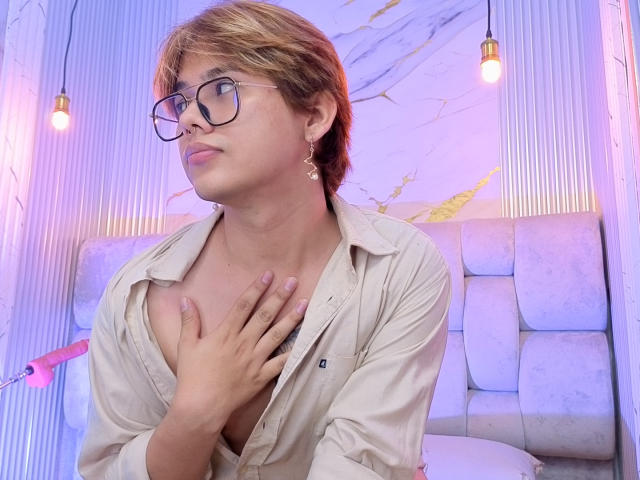 BenjiVampire, short brown hair, glasses, light beige shirt, hand on chest, pink nipples, pink dildo in background, light purple and pink lighting, looking to the side, confident.