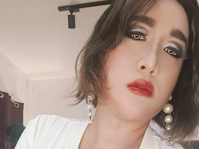 OhhhMyMistress with shiny eyeshadow, red lipstick, and pearl earrings, has short brown hair and white shirt, looking directly at camera with a slightly pouty expression.