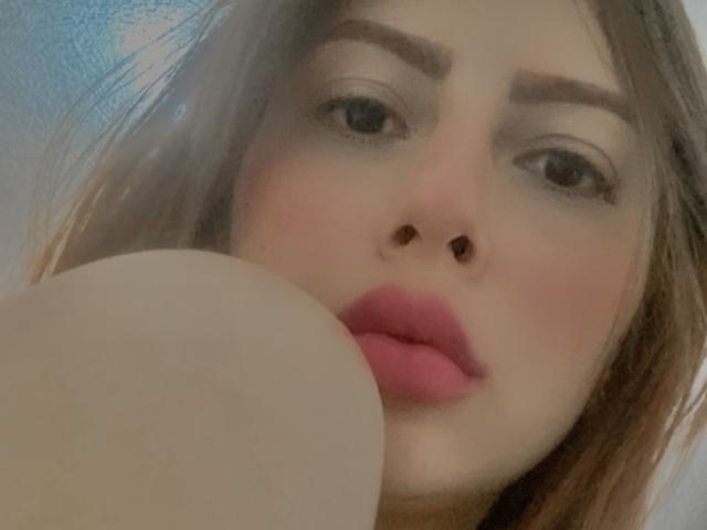 Viooletta69's face with pink lipstick, brown eyebrows, and light skin. Her nose is centered, and her pink pout is near a large, pale, round butt in the foreground.