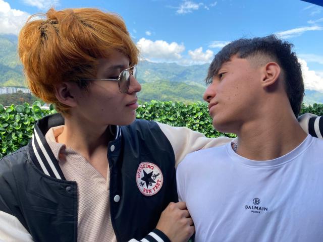 MaxAndTed with orange hair and glasses in a black and white varsity jacket, looking at MaxAndTed with short black hair in a white Bamim shirt. Both have serious expressions.
