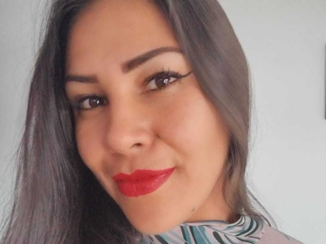 KimmyHolleshot has dark brown eyes, red lipstick, and long straight black hair with subtle highlights. She's smiling slightly with a cute, confident look.