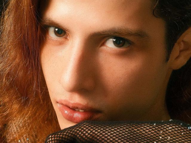 AllenClark's face with brown wavy hair, serious brown eyes, and slightly parted glossy lips, wearing a black mesh garment, showing subtle facial freckles and smooth skin.