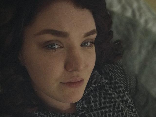 MrsXSweet has pale skin, blue eyes, and curly brown hair, wearing a herringbone pattern shirt, looking slightly up with a subtle smile. Her tits are not visible.