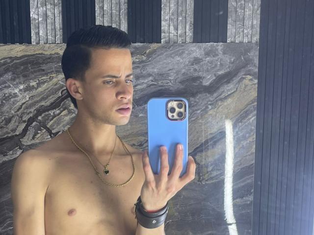 AxelBigCock, shirtless, holding blue phone, gold necklace, black wristbands, looking in mirror, short dark hair, slight facial expression, marble wall, reflection, medium skin, slight chest, clean look.