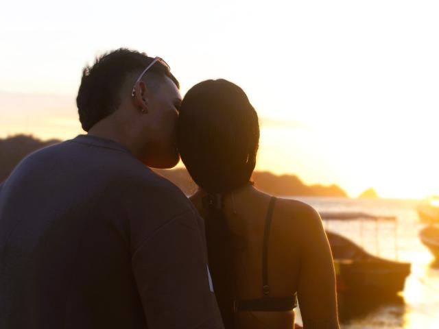 ZairaAndres and a dude kissing at sunset, she's in a black bra, his back's to the camera, she's got her head turned, he's got glasses, boat in water.
