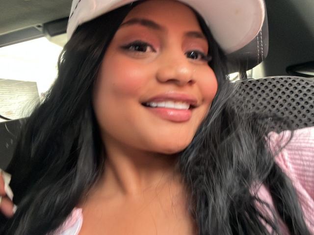 MichelleVain has long black hair, brown eyes, pink eyeshadow, and a smile showing white teeth. She's wearing a white cap and pink shirt, looking cute and sexy.
